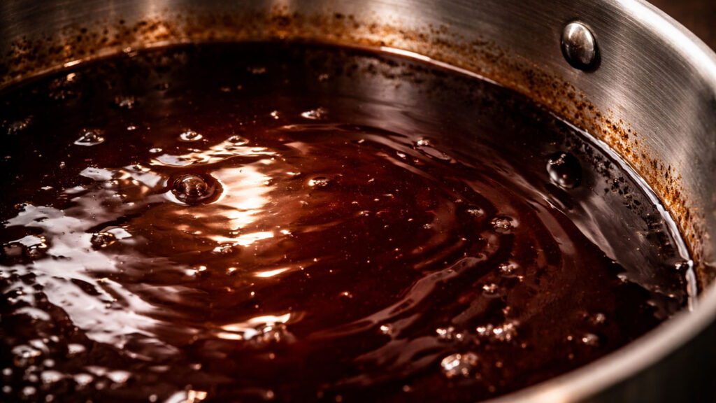 Close-up of glossy reduced red wine sauce with deep ruby color in stainless steel pan.