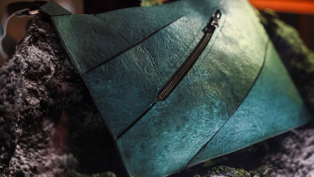 Close-up texture of a teal-toned biotech leather handbag made from lab-grown T-Rex collagen designed by Enfin Levé.